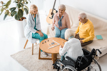Young Female Nurse Playing Domino With Senior Patients In Nursing Home