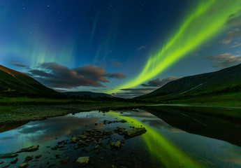 aurora borealis in the night sky cut the mountains, reflected in the water.