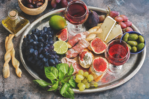 Fotografía A variety of appetizer, prosciutto, grapes, wine, cheese with mold, figs, olives on a metal tray