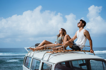 young couple with sunglasses sitting on top of minivan roof