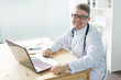© satura_ - Healthcare, medical and people concept - Smiling doctor sitting at table with laptop and looking at the camera