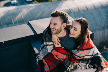 Wall Mural - high angle view of laughing young couple covered in plaid sitting on rooftop together