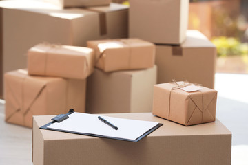 Clipboard, parcel with tag and blurred stacked boxes on background, indoors