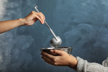 Volunteer putting food into bowl of poor woman on color background, closeup. Concept of help