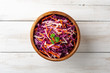 Fresh coleslaw salad with red and white cabbage and carrots in bowl on white wooden background. Top view. Copy space.