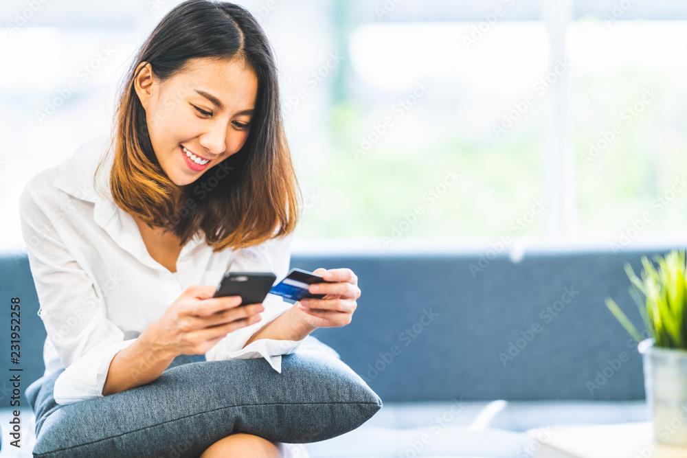 Young beautiful Asian woman using smartphone and credit card for online shopping at home with copy space. E-payment technology, shopaholic lifestyle, or mobile phone financial application concept - obrazy, fototapety, plakaty 