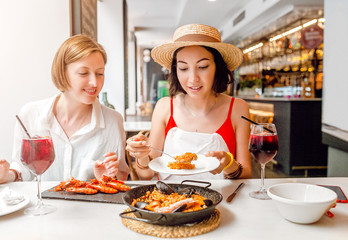 Two happy cheerful girl friends drinking wine and having lunch at seafood restaurant