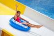 Beautiful girl on inflatable ring riding water slide with hand up in aqua park