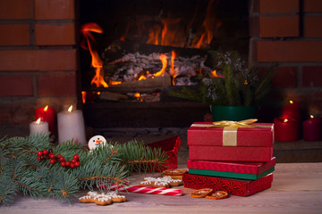 Wall Mural - Christmas decorations, gifts and cookies on wooden table beside cosy open fire place. Winter holidays concept