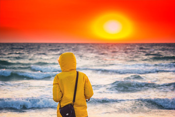 Wall Mural - Beautiful sunrise above the stormy sea with girl in the hood looking into the distance, seascape