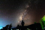 Fototapeta Kosmos - Silhouette of a standing human looking milky way at the night time