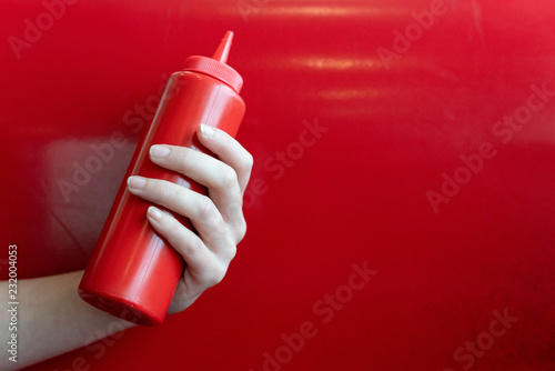 Cuadros en Lienzo Hand holding a ketchup bottle on a red background in a diner