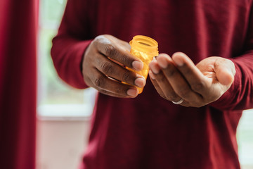 african american man in red shirt pouring pills from prescription pill bottle