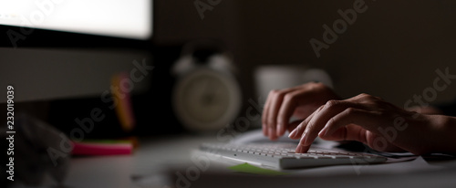 Fotomural Workaholic hand typing keyboard in dark late night with computer screen light, clock, coffee cup and stuff on desk table with noir working in workplace or hacker cyber crime concept