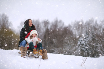  A winter fairy tale, a young mother and her daughter ride a sled in the forest. A girl on a sled with gifts on the eve of the new year in the park. 