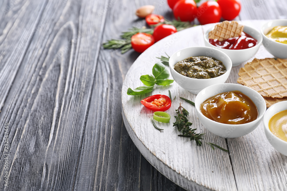 Different tasty sauces in bowls with waffles on wooden table