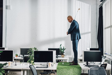 side view of young african american businessman playing golf on table in office