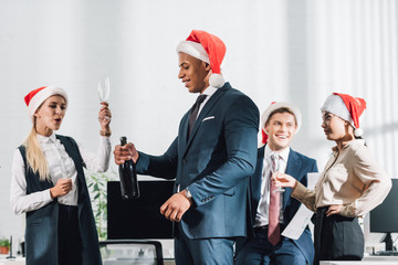 Wall Mural - happy young multiracial business colleagues in santa hats celebrating christmas in office