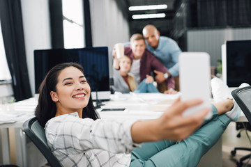 Wall Mural - smiling young businesswoman taking selfie with smartphone in open space  office