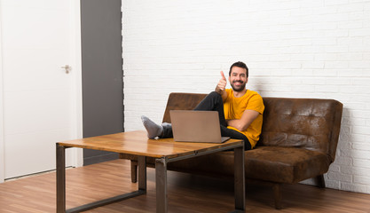 Man with his laptop in a room giving a thumbs up gesture because something good has happened