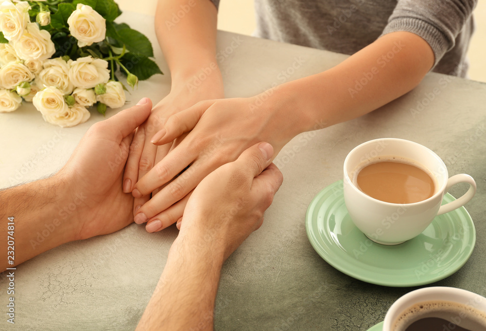 Loving young couple holding hands on light table, closeup