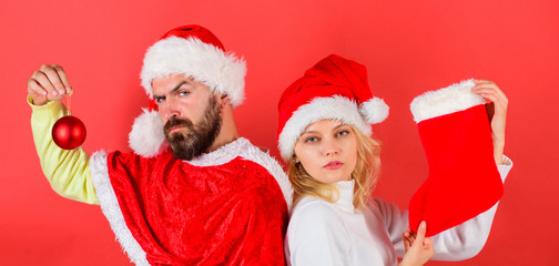 Wall Mural - Christmas stocking tradition. Couple christmas santa costume hold sock and ornament ball. Woman and bearded man in santa hat waiting christmas red background. Christmas celebration concept