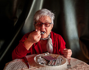 Concept of medicine and health care. A senior woman with her plate full of pills tablets and eating pills with a spoon