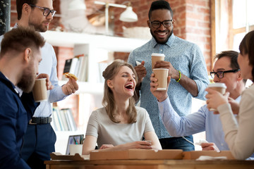 Wall Mural - Happy diverse colleagues have fun at lunch break in office, smiling multiracial employees laugh and talk eating pizza and drinking coffee, excited workers celebrate shared win ordering takeaway food