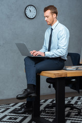 serious businessman sitting on table and working on laptop in modern office