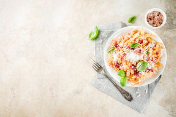 Italian food, fusilli pasta with  tomato sauce, grated parmesan cheese and basil, light stone table copy space top view