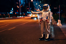 Spaceman Standing On A Street In The City At Night Hitchhiking