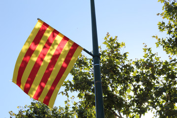 An Aragon region flag, with red and yellow stripes, hung on a light pole with a blue sky during a sunny summer day in Ejea de los Caballeros, Spain