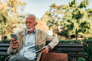 Retired man using phone while sittig on the bech.