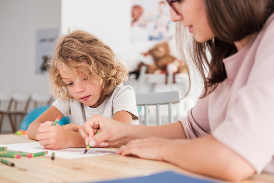 close-up of a child with an autism spectrum disorder and the therapist by a table drawing with crayo