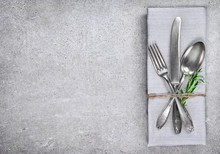 Table Setting Background With Copy Space. Concrete Background With Napkin, Silverware And Rosemary Branch. Cutlery With Fork, Knife And Spoon. Top View.