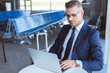 © LIGHTFIELD STUDIOS - adult serious businessman in glasses typing on laptop in airport