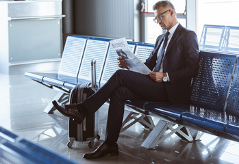 Wall Mural - adult businessman sitting at departure lounge at airport and reading newspaper