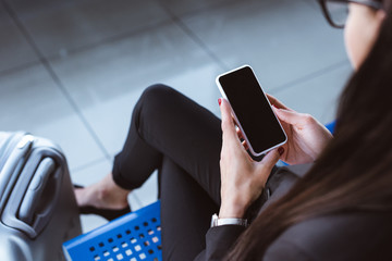 Wall Mural - young businesswoman sitting at departure lounge in airport and holding smartphone