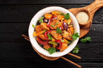 Wall Mural - Stir fry with chicken, vegetables, soy sauce and sesame on black wooden background. 