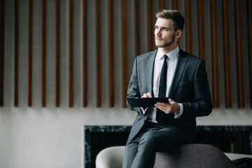 Wall Mural - Young handsome man sitting in office with cup of coffee and working on project connected with modern cyber technologies. Businessman with notebook trying to keep deadline in digital marketing sphere.