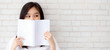 Banner website beautiful portrait asian woman happy hiding behind open the book with cement or concrete background, girl standing reading for learning, education and knowledge concept.