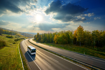 three white buses traveling on the asphalt highway between deciduous forest in autumn colors under t