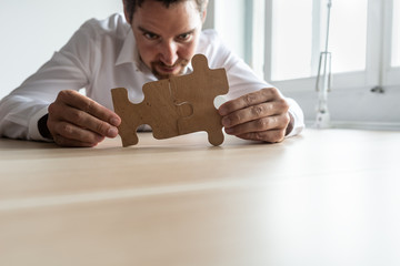 Wall Mural - Focused young businessman joining two matching puzzle pieces