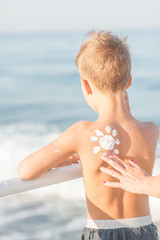 Mom draws on the shoulder of his son the sun with sunscreen