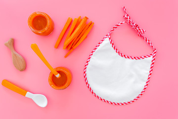 Healthy food for small babies. Carrot puree in bowl near bib, carrot slices, spoon on pink background top view