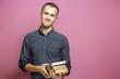 Young man holding a stack of books on a pink background.