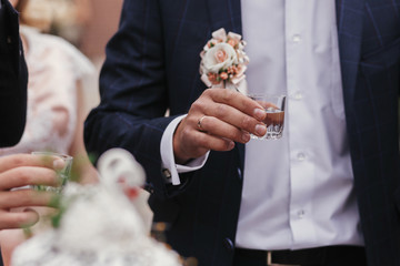 Sticker - Stylish man holding glasses of vodka and toasting at wedding reception. Corporate businessman cheering with alcohol drinks at party outdoors. Christmas feast