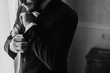 © sonyachny - Stylish groom putting on suit and bow tie at window light. Confident and happy portrait of man. Groom getting ready in morning. Creative wedding photo