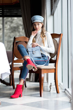 Beautiful Young Girl In Red Boots, Fashionable Clothes And Blue Colored Cap. The Girl In The Restaurant. Trend Clothing. Without Filters. Natural Color.