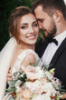 © sonyachny - Gorgeous bride and stylish groom gently hugging and smiling on background of green trees. Sensual wedding couple embracing. Romantic moments of newlyweds. Wedding photo